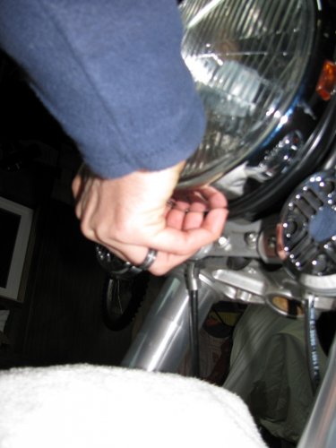 Fingernails help here.
Put your fingers between the headlamp bucket and the chrome headlamp ring and pull the bottom of the headlamp out.  It only needs to travel a centimeter or two for it to be free.  Unhook the top and carefully lay the headlamp on the fluffy towel you placed on the fender (that's a hint).
