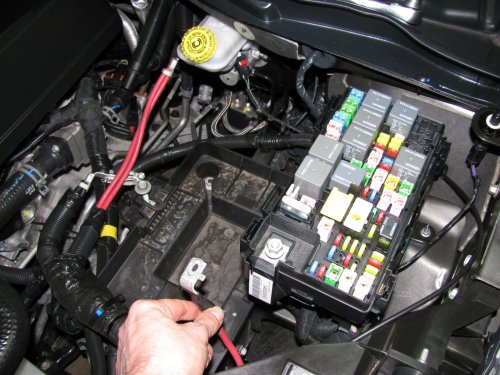 To make life MUCH easier just remove the battery.  Also remove the positive power lead (red wire I'm holding) from the fuse box as well as the cover.
