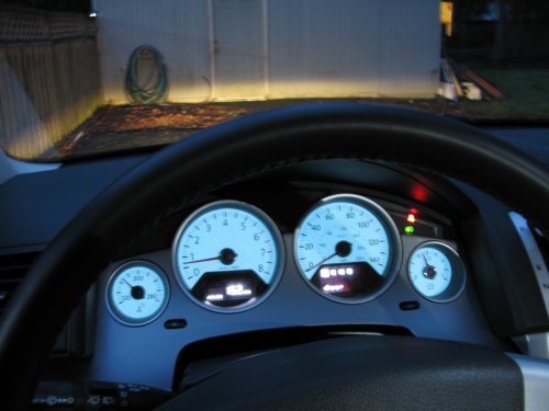 View from the driver's seat with the fogs on.  Notice the green "fog lights on" indicator to the right of the speedometer and below the red "fasten seat belt" indicator.  I just finished adjusting the fog lights.  The top of the light you see on the building wall is 14".  If I went by the instructions it would've been 13" but I wanted just a little more distance.

