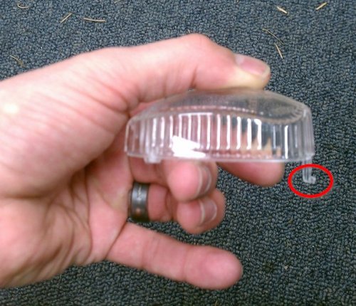 The red circled part shows why the lens needs to be angled out when removing it.  That hook helps hold the lens in to the housing.  The end opposite the hook is where the screw goes.
