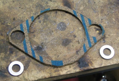 Solution:  1/8" cork gasket with a 1/16" stainless-steel washer under each mounting ear.  This is a spacer, not really a gasket.  The gasket material is used to hold the washers (well, along with some Gas-A-Cinch) and help prevent the mounting ears from getting torque stress during starting.
