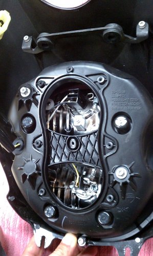 Remove the headlight and place on a thick towel.  The low-beam is at the top of the headlight, which is the top of this picture.  This shows the back removed and the bulb area exposed -- there are 7 screws that hold the back on.  The greyish-silver bolt at the 11 o'clock position on the outside edge is the headlight vertical adjustment.  To get more operating space inside the housing I rotated mine anti-clockwise 6 turns.  Make sure you mark the bolt with a spot on the housing so you know where to return it when everything is all installed.
