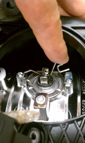 Push the retaining clip down and then to the top of the light housing, then pivot it up and out of the way to the left side of the light housing.
