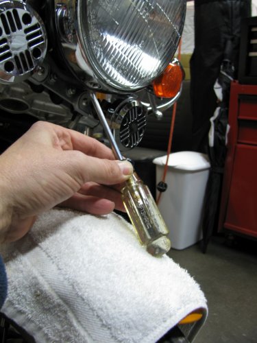 Use a Phillips screwdriver to remove the retaining screw at the bottom of the headlamp.  No need to completely remove the screw, just until it becomes loose & wobbly.
