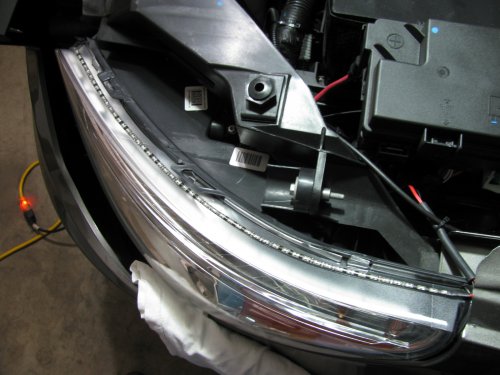 Applying the LED array to the head light.
I started from the top (right side of picture) and carefully removed the LED backing tape as I move towards the front of the head light.  Just eye-balled the application but kept it more towards the inside of the light (engine side).  This allows more light to be spread out onto the head light lens and disperse the light.  I put a rubber tube around the wires to protect them from chaffing against the metal.  Be sure to clean the lens well!  I used rubbing alcohol and a clean rag.
