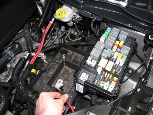 To make life MUCH easier just remove the battery.  Also remove the positive power lead (red wire I'm holding) from the fuse box as well as the cover.
