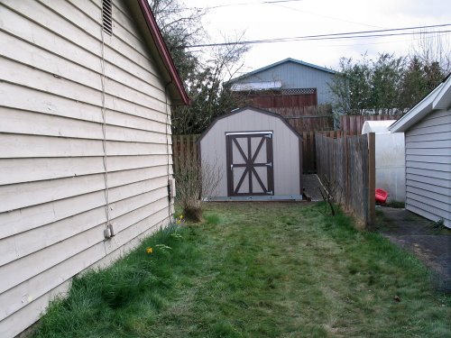 Finished.  View from side of house.  The sheds come with a sturdy, locking door.  The door is wide at 45.5" (1.16m), and 70" (1.78m) in height, and swings very easily.  I like the width but a taller door would've been a definite plus.
