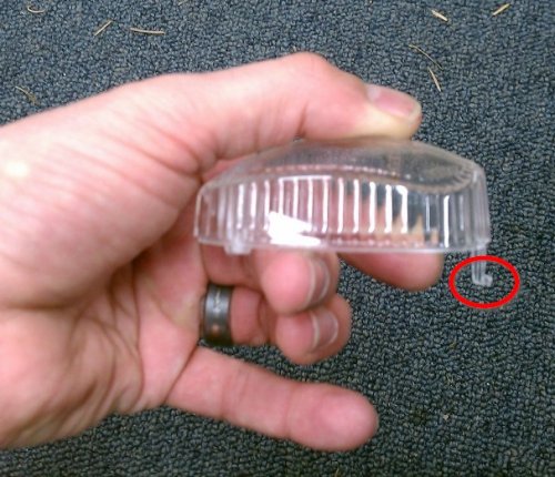 The red circled part shows why the lens needs to be angled out when removing it.  That hook helps hold the lens in to the housing.  The end opposite the hook is where the screw goes.

